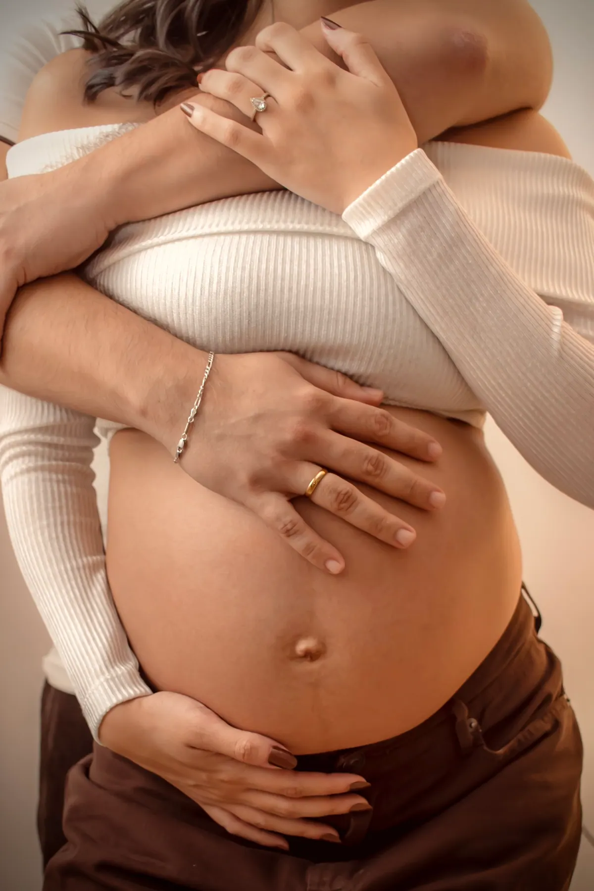 Detalhe das mãos do casal sobre a barriga da gestante