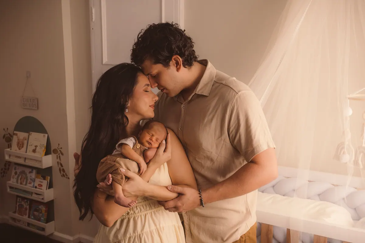 Pai e mãe abraçados segurando o bebê recém-nascido no quarto do bebê