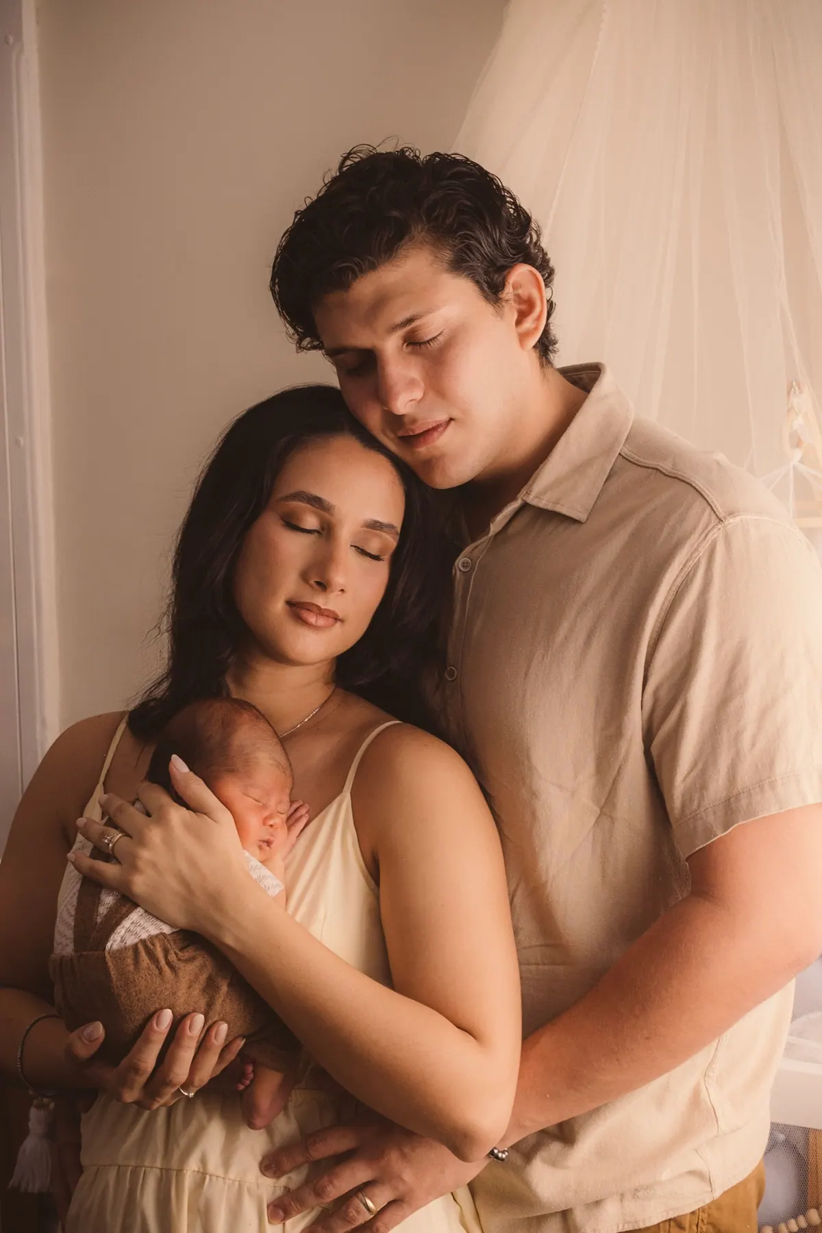 Casal abraçado com o bebê recém-nascido no colo da mãe, em luz suave