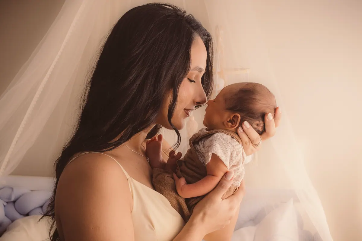 Mãe segurando o bebê recém-nascido nas mãos e olhando para ele com carinho
