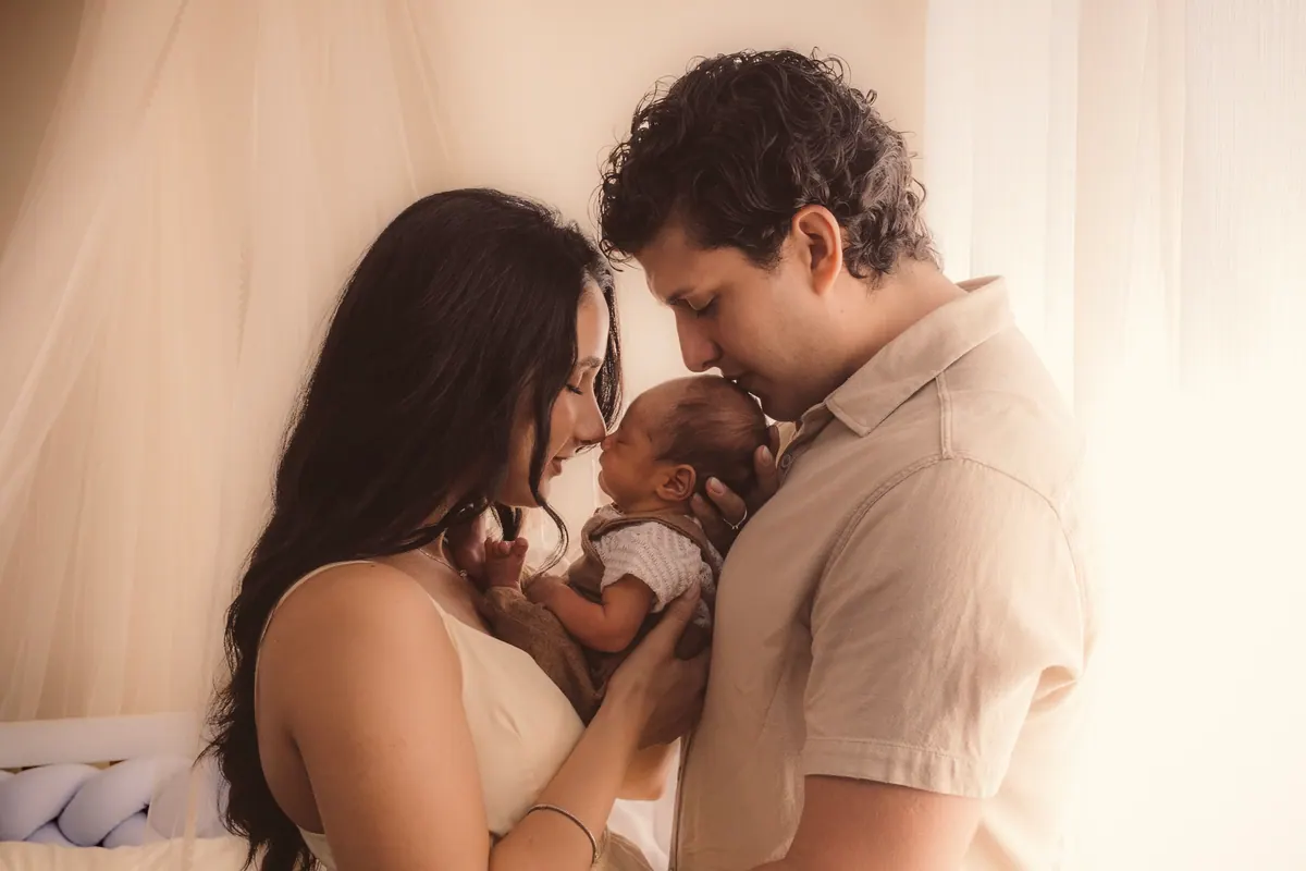 Pai e mãe encostando os narizes enquanto seguram o bebê recém-nascido